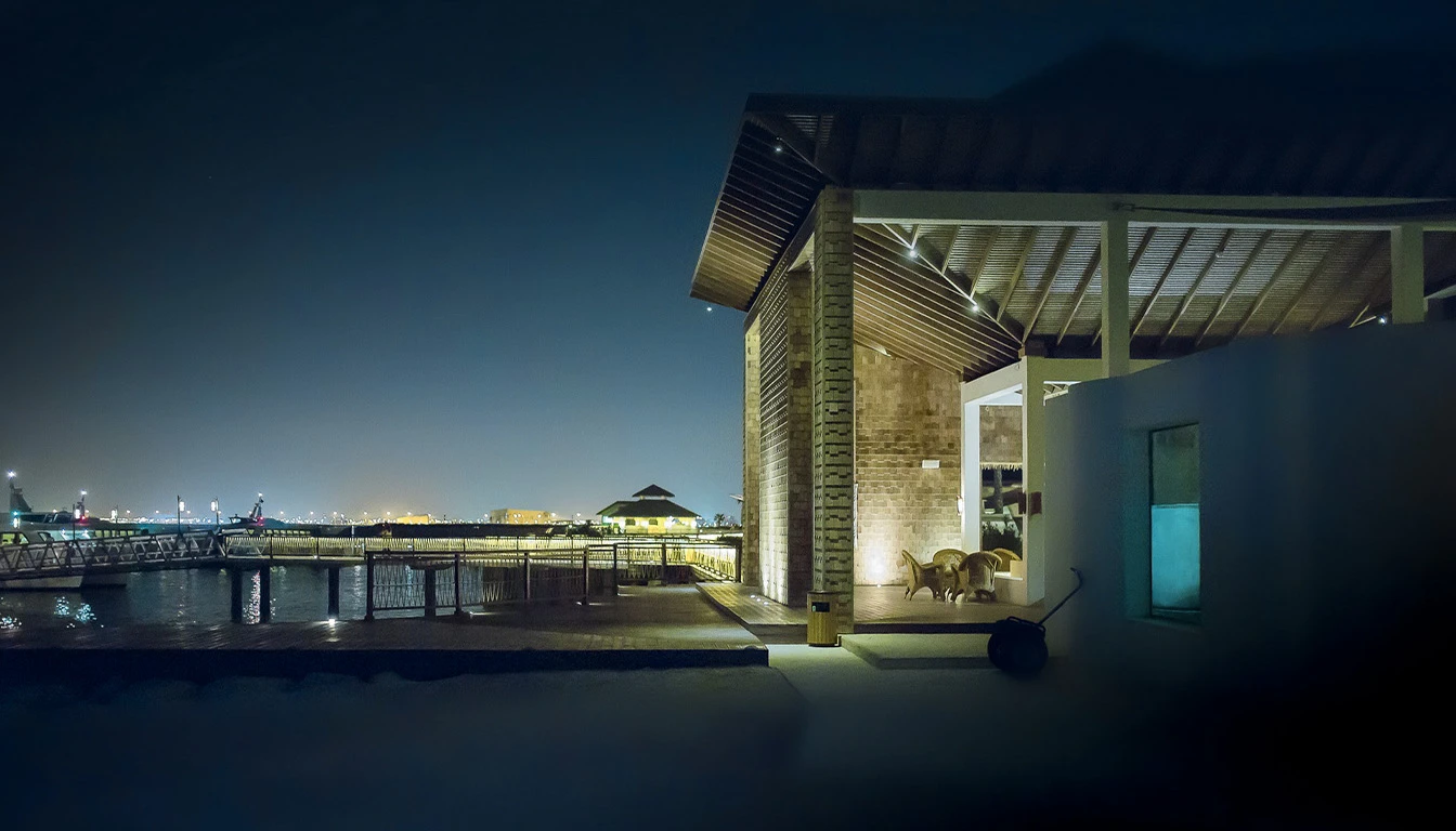 Scène urbaine nocturne avec bâtiment moderne illuminé à structure courbe en lamelles de bois, façade vitrée et éclairage ambré