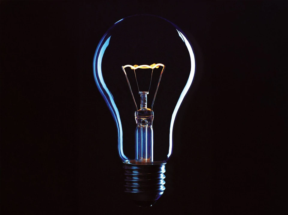 Mains tenant deux ampoules électriques sous un luminaire suspendu noir sur fond neutre